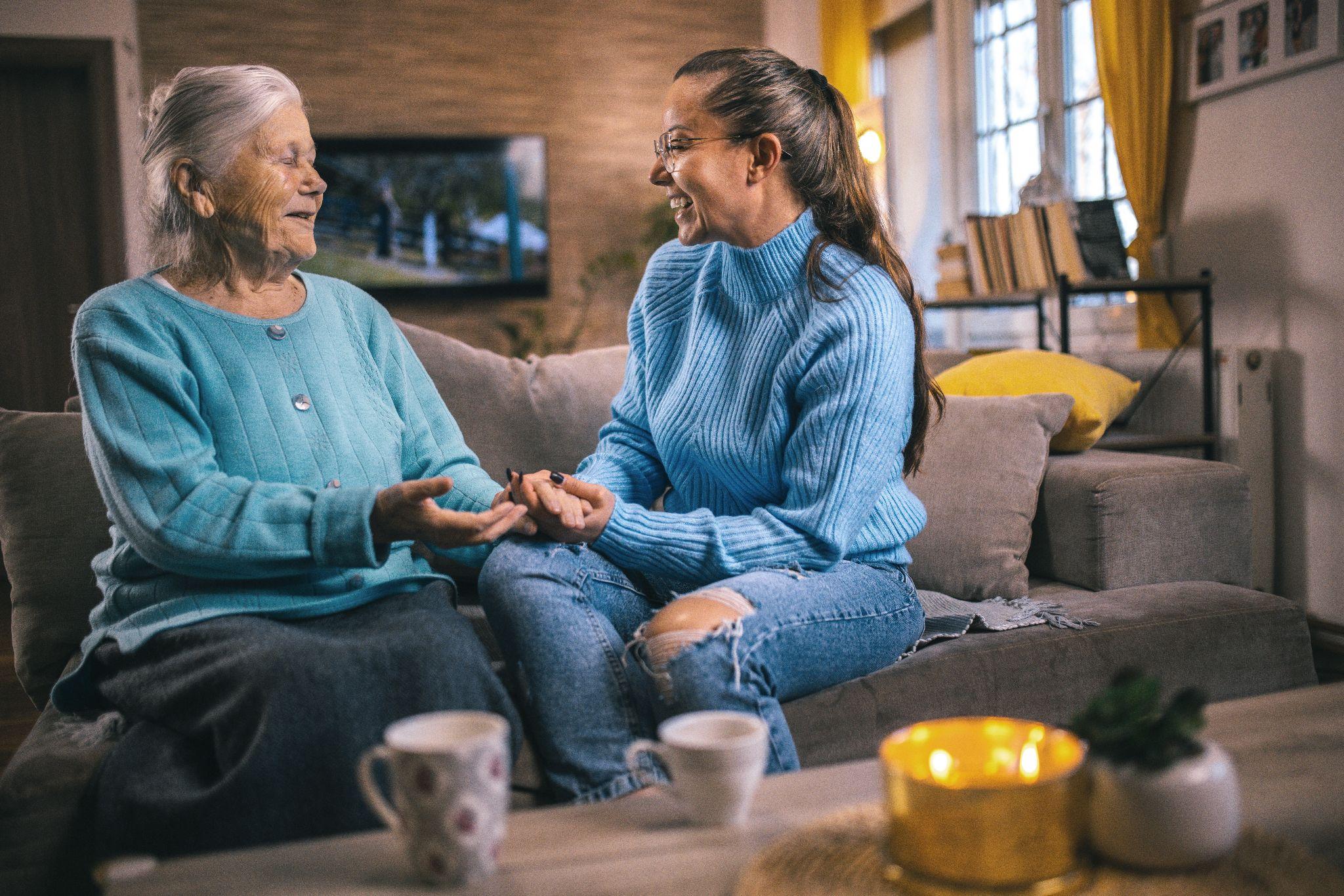 An elderly woman and an older adult speaking to eachother over a cup of tea.